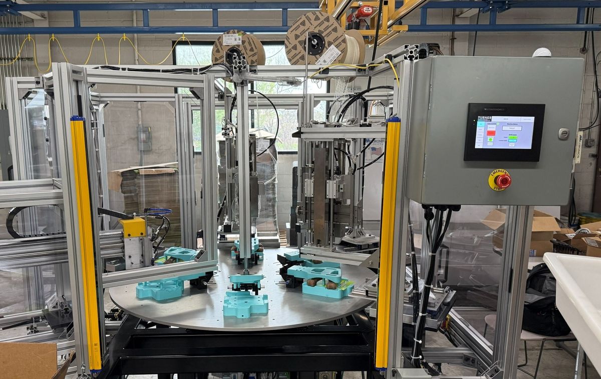 The rotary indexing elastic stapling machine built by TMD, with an aluminum extrusion frame, light-curtain guarding at the operator face and an HMI at the load station.