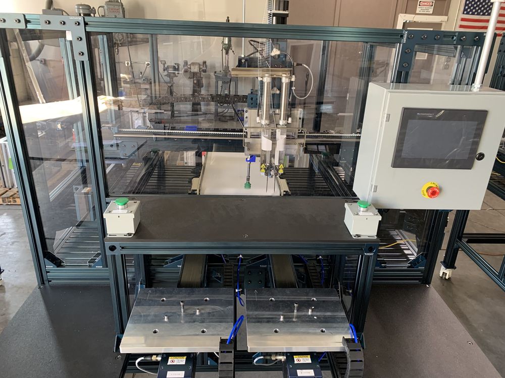 The 6-axis elastic stapling machine on the shop floor — extruded aluminum frame, polycarbonate guarding, fixture plates at the infeed and an operator HMI mounted at the right-hand side.