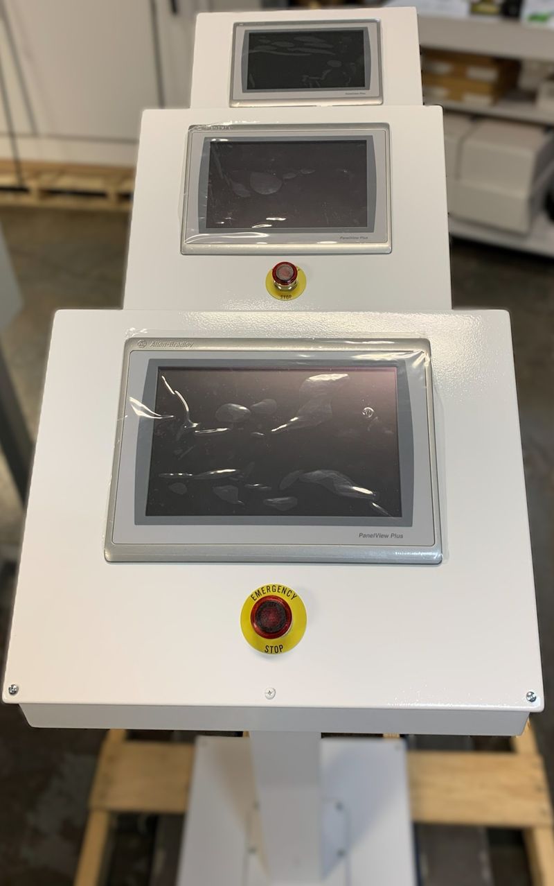 Three operator HMI enclosures with touchscreens and emergency-stop buttons, built and staged in the shop.