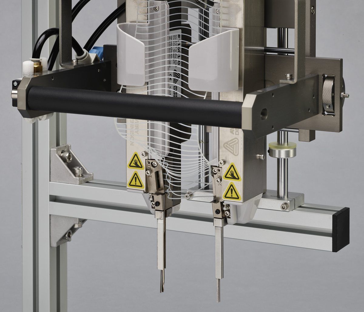 Close view of the IndES applicator head — twin needles below the reel-fed staple magazine, with the guard and caution labels in place.